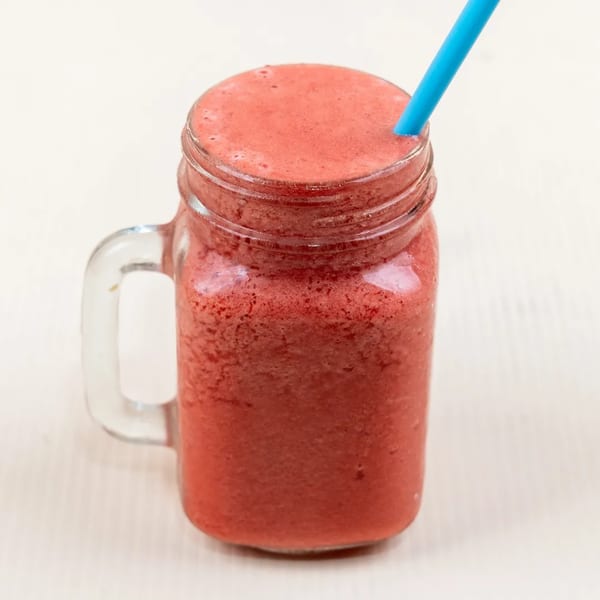 A vibrant red smoothie in a mason jar with a blue straw, on a light background.