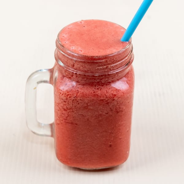 A vibrant red smoothie in a glass jar with a blue straw, from The Little Coffee Shoppe.