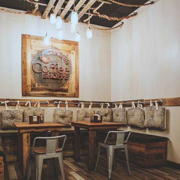 Rustic coffee shop interior with wooden tables, metal chairs, and a "Coffee Shoppe" sign.