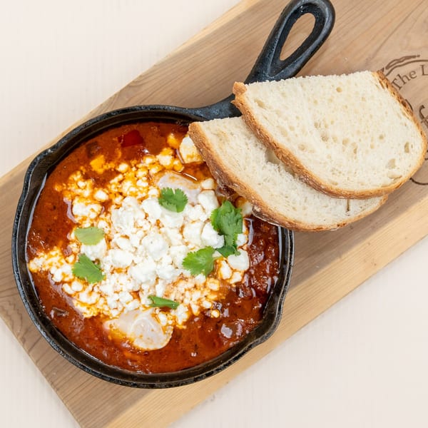 Shakshuka in a cast iron skillet with feta cheese, cilantro, and two slices of bread.