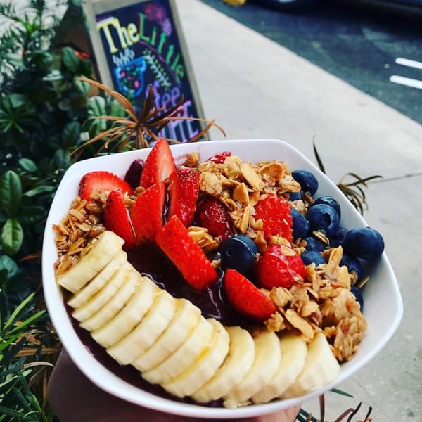 A vibrant acai bowl with sliced bananas, strawberries, blueberries, and granola, held outdoors.