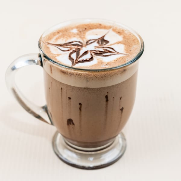 A clear mug of mocha with latte art and chocolate drizzle, from The Little Coffee Shoppe.