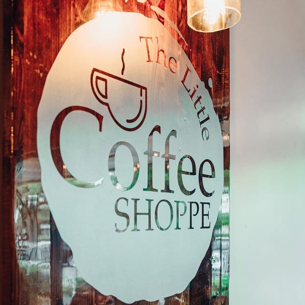 The Little Coffee Shoppe logo, a coffee cup icon and text, on a frosted glass door.
