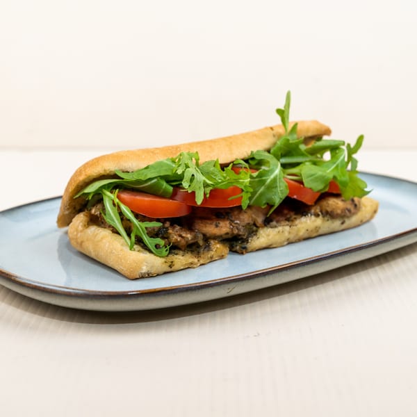 A chicken pesto sandwich with tomatoes and arugula on a baguette, served on a blue plate.