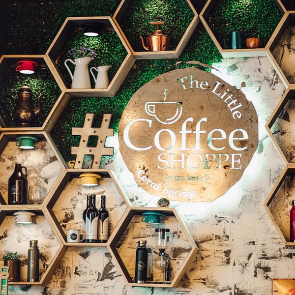 Hexagonal shelves with coffee-related items and a lit "The Little Coffee Shoppe" sign.