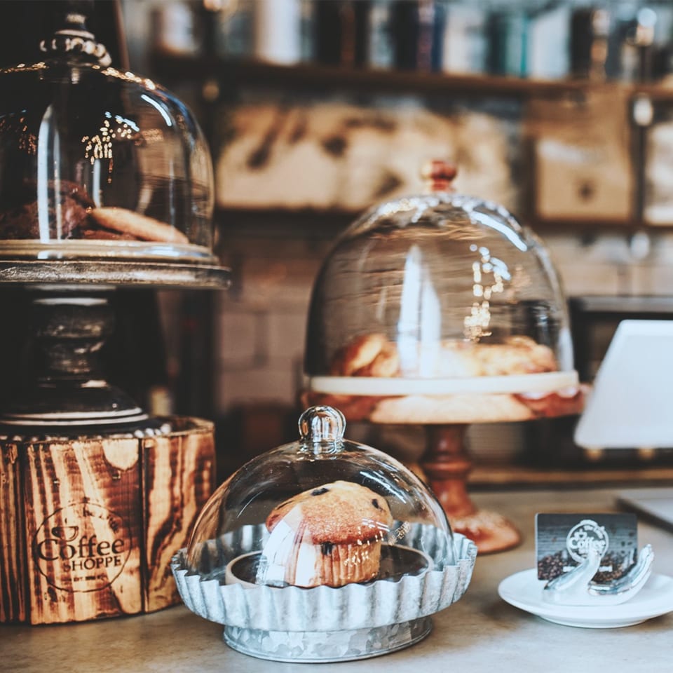 Assortment of pastries, including a blueberry muffin, displayed under glass cloches at The Little Coffee Shoppe.
