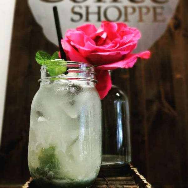 Iced mint lime drink in a mason jar with a black straw, next to a pink rose.