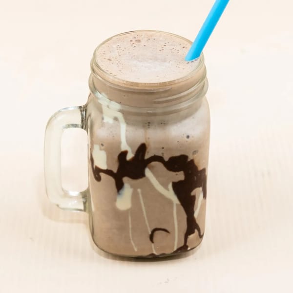 A chocolate milkshake in a mason jar with a blue straw, drizzled with chocolate and white syrup.