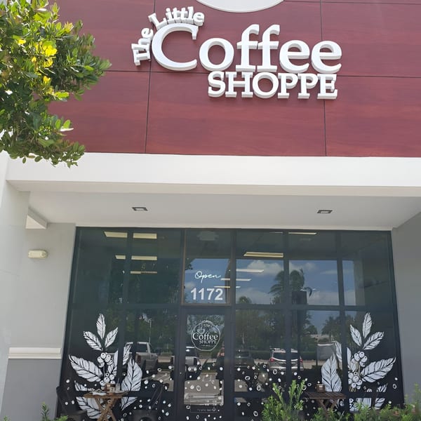 The Little Coffee Shoppe storefront with a red facade, large windows, and coffee bean plant decals.