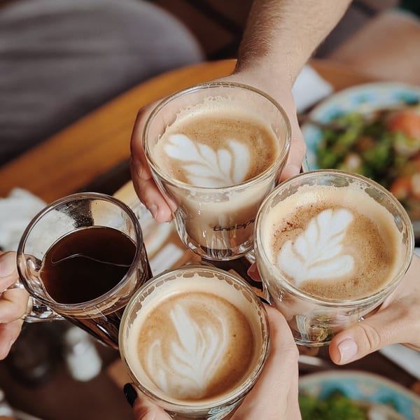 Four people holding various coffee drinks, including lattes with art and black coffee, in a toast.